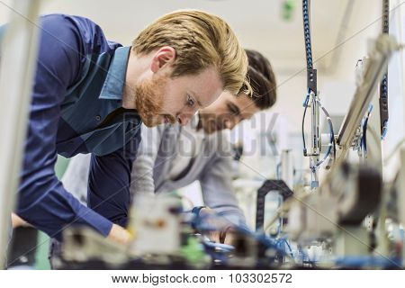 Two Young Handsome Engineers Working On Electronics Components