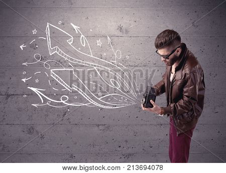 A hipster guy opening his point of view through looking a vintage camera concept with illustratied drawn arrows on urban wall