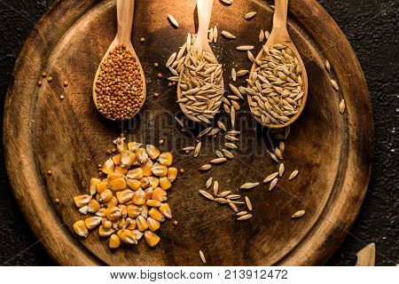 Top view of corn, millet, barley and oat grains in wooden spoons on round wooden tary