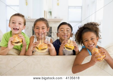 Four Young Children Eating Cheeseburgers In Living Room Smiling