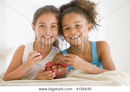 Two Young Girls Eating Strawberries In Living Room Smiling