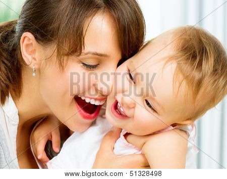 Mother and Baby kissing and hugging at Home. Happy Smiling Family Portrait. Mom and Her Child Having Fun together