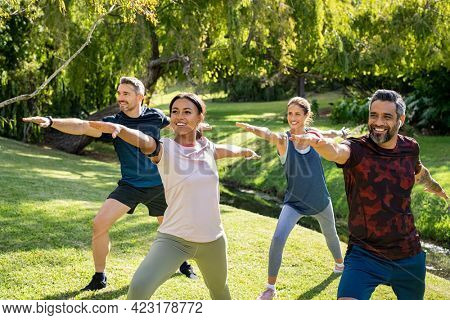 Mature multiethnic couple doing sport and physical exercises outdoor with friends. Group of active mature man and beautiful mid adult women doing workout at park in the afternoon. 