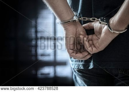 Arrested man in handcuffs with handcuffed hands behind back in prison