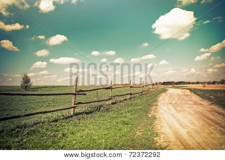 Sunny Day In Countryside. Empty Rural Road Going Through Summer Landscape Under Blue Cloudy Sky