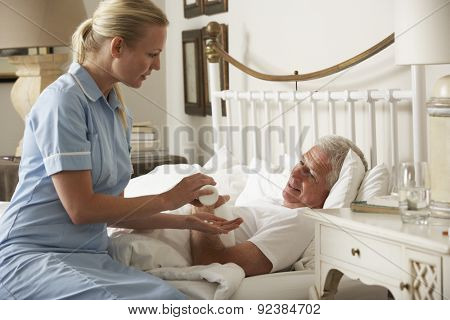 Nurse Giving Senior Male Medication In Bed At Home