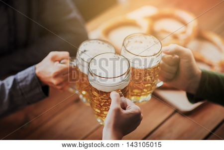 people, leisure and drinks concept - close up of hands clinking beer mugs at bar or pub