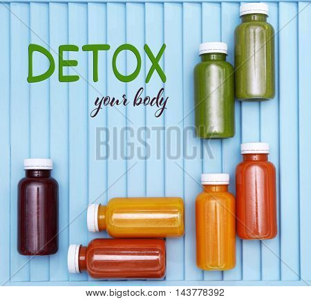 Bottles with delicious detox drinks and text detox your body on blue wooden background. Detox diet concept.