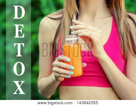 Woman holding bottle with delicious detox drink. Text detox on blurred background. Detox diet concept.