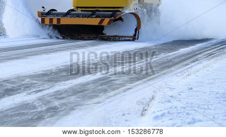 Snowplow removes snow off icy road in winter.