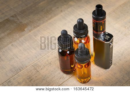 Vaping hardware and juice.  Vape e-juice with mod and bottles with child proof lids over wood background.