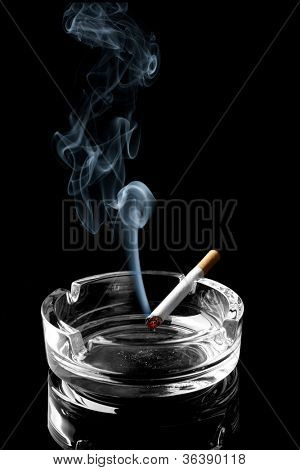 Closeup of cigarette on ashtray with wisp of smoke