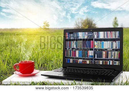 Laptop and cup of hot coffee on the background picturesque nature, outdoor office. E-book library concept with laptop computer and book. Old books on a wooden shelf. Travel concept. Business ideas.