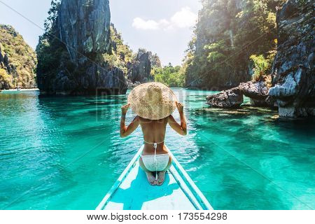 Back view of the young woman in straw hat relaxing on the boat and looking forward into lagoon. Travelling tour in Asia: El Nido, Palawan, Philippines.