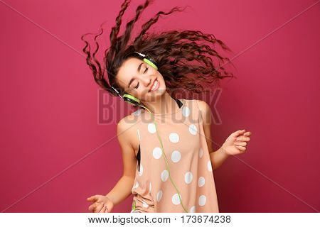 Beautiful young woman in headphones listening to music and dancing on color background