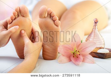 Close Up Of Hands Doing Foot Reflexology Massage On Female Foot. Flower, Candle And Massage Oil Next