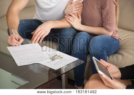 Renting and tenancy concept. Close up of couple in love signing rental agreement sitting on couch with female realtor, starting living together, housing rent, residential property lease contract