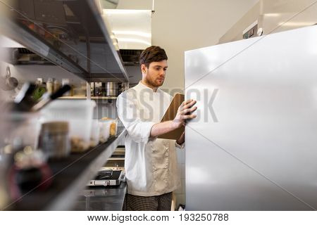 cooking, profession and people concept - male chef cook with clipboard doing inventory in restaurant kitchen fridge