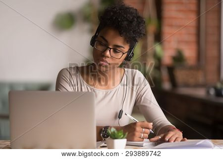 Focused Mixed Race Woman Wearing Headphones Watching Webinar Write Notes