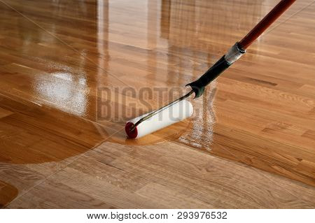 Lacquering Wood Floors. Worker Uses A Roller To Coating Floors. Varnishing Lacquering Parquet Floor 