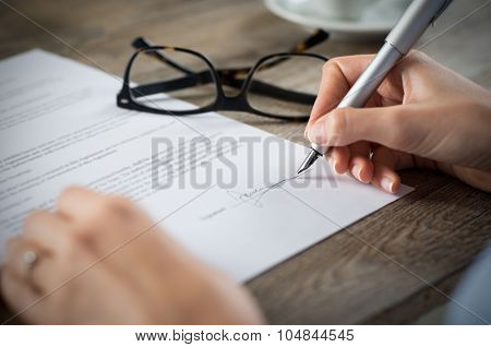 Closeup shot of a woman signing a form. She's writing on a financial contract. Shallow depth of field with focus on tip of the pen.
