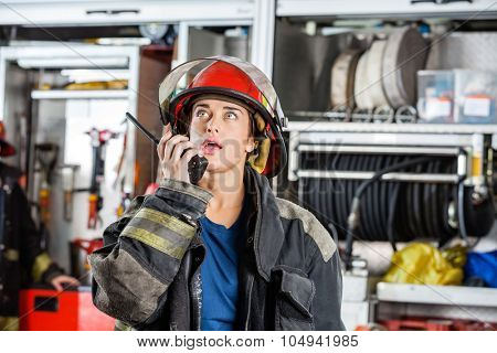 Confident female firefighter looking up while using walkie talkie at fire station