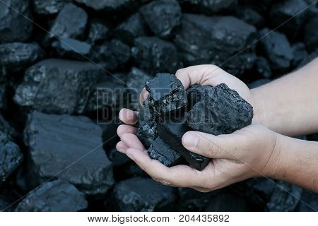 Coal mining - hands holding sunlit dark coal stone part. Concept coal mining coal processing energy source environment protection.