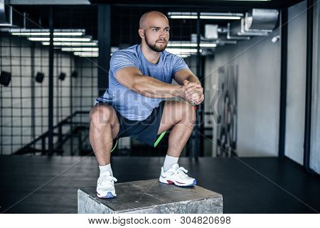 Man Doing Squats On A Squat Box At The Gym. Guy At The Gym Working Out Standing On A Wooden Squat Bo