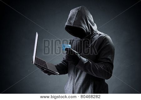 Computer hacker with credit card stealing data from a laptop concept for network security, identity theft and computer crime