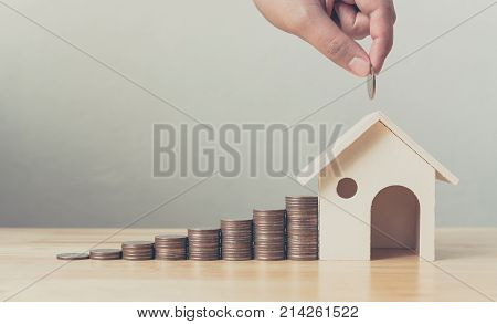 Property investment and house mortgage financial concept Hand putting money coin stack with wooden house