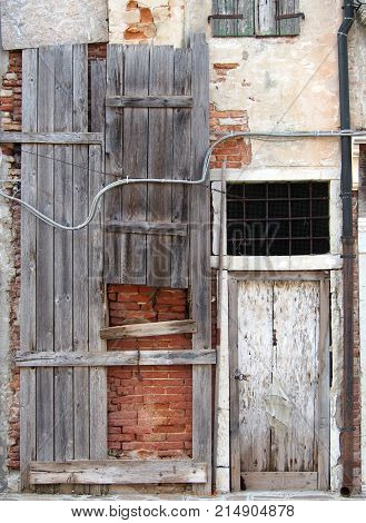 abandoned board up derelict house with padlocked door and decaying brick walls in italy