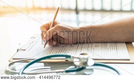 Medical Doctor Writing On Patient Personal Health Care Record Discharge Form, Or Prescription Paperw