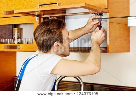 Handyman fixing kitchen's cabinet with screwdriver