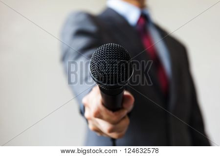 Man in business suit holding a microphone conducting a business interview, journalist reporting, public speaking, press conference, MC