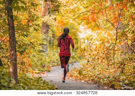 Run woman jogging in outdoor fall autumn foliage nature background in forest. Trail running runner athlete training cardio outdoors, orange colors tree leaves.