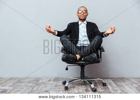 Relaxed handsome african young man sitting and meditating on office chair