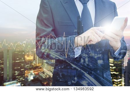 Double exposure of professional businessman using smart phone and blurred city centre of business with trading graph chart Technology & Business trading concept