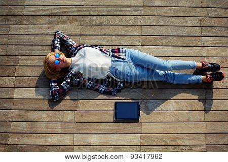 Attractive student lying on the wooden floor with a tablet enjoying the good weather and the sun