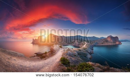 Amazing summer landscape with mountains sea blue sky sun and beautiful colorful red clouds at sunset in Crimea. Sunset in mountains. Panoramic. Nature background. Vibrant landscape in twilight.