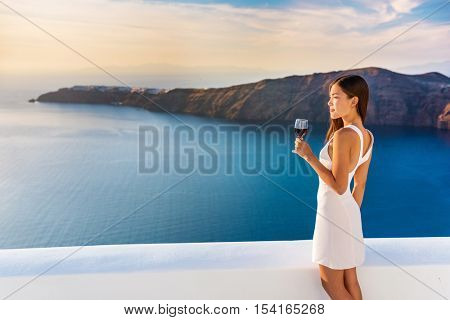 Luxury hotel terrace. Europe destination summer vacation. Asian woman drinking red wine relaxing enjoying view of the mediterranean sea in Oia, Santorini, Greece. Honeymoon high end travel holiday.