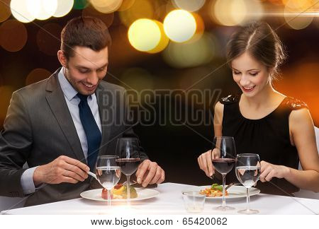 restaurant, couple and holiday concept - smiling couple eating main course with red wine at restaurant