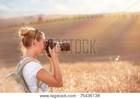 Happy traveler girl photographing ripe wheat field in bright sun rays, autumn harvest season, interesting profession, travel and tourism concept