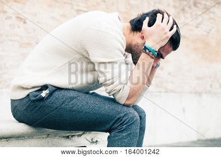 Problems and stress, stressed man. A young man with his hands in the hair sitting on a bench outdoors. Concept of problems, stressful thoughts, difficulty and crisis.