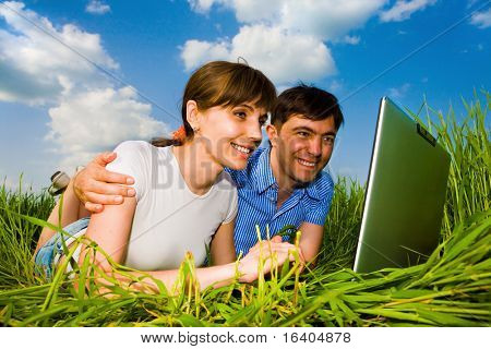 Casal feliz ocasional em um computador laptop ao ar livre. Coloque sobre a grama verde.