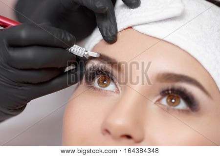 Permanent makeup eyebrows. Mikrobleyding eyebrows workflow in a beauty salon. Cosmetologist applying a special permanent makeup on a woman's eyebrows.