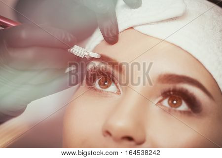 Permanent makeup eyebrows. Mikrobleyding eyebrows workflow in a beauty salon. Cosmetologist applying a special permanent makeup on a woman's eyebrows.