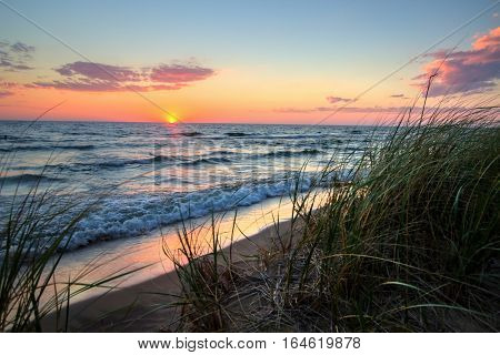 Tranquil Sunset Beach Background.  Beautiful sunset horizon over water with a sandy beach and dune grass in the foreground. Hoffmaster State Park. Muskegon, Michigan.