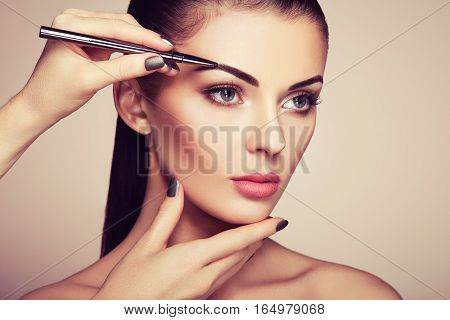 Beautiful brunette woman paints the eyebrows. Beautiful woman face. Makeup detail. Beauty girl with perfect skin