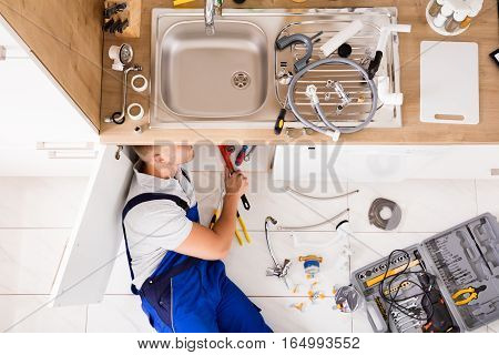 High Angle View Of Male Plumber In Overall Fixing Sink Pipe