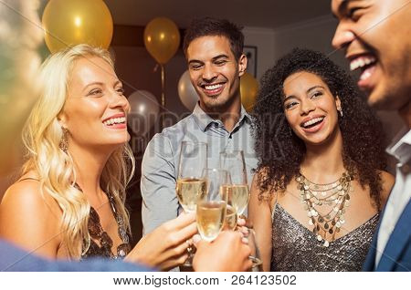 Group of five multiethnic friends enjoying at house party. Young men and beautiful women holding wine glasses raising toast. Cheerful smiling girls and guys celebrating at home with champagne.